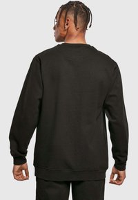 Il pullover nero presenta un collo rotondo, maniche lunghe, una texture morbida e polsini a costine. La vista posteriore mostra una vestibilità ampia e rilassata.
