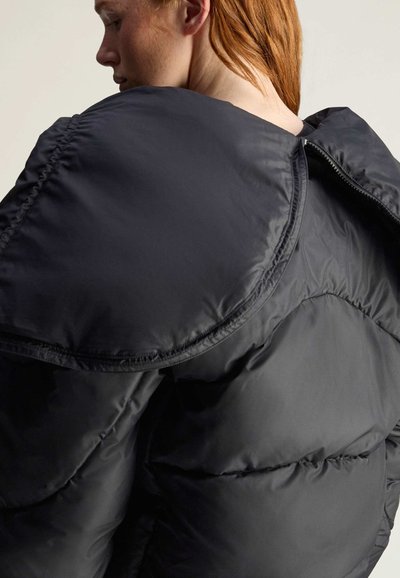 Czarna kurtka puchowa z wysokim kołnierzem i oversize'owym krojem. Posiada pikowaną fakturę oraz zamek błyskawiczny z tyłu, wykonana z lekkiego materiału.