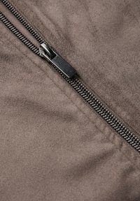 Brun mocka tyger med en metallisk dragkedja som löper längs ena sidan, med en texturerad yta och släta hårdvarudetaljer.