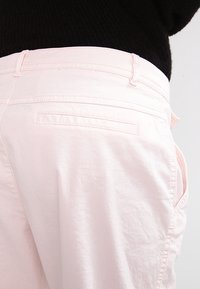 Ljusrosa bomullbyxor med en avslappnad passform. Funktioner inkluderar sidofickor och en enda bakficka med minimala sömnadsdetaljer.