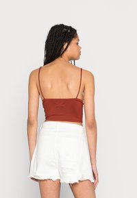 Top cropped bordô com alças finas, combinado com calções brancos desgastados com bordas desfiadas e bolsos posteriores.
