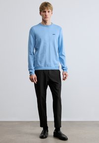 Világoskék pulóver kerek nyakkal és bordás mandzsettával, fekete nadrággal és fekete cipővel párosítva. Egyszerű dizájn és puha textúra.