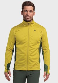 Gelbe Zip-Jacke aus strukturiertem Stoff, mit grünen Seiteneinsätzen, Daumenlochärmeln und einem geprägten Logo auf der Brust.