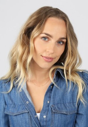 Denimhemd aus leicht blauem Stoff, mit Knopfleiste, Brusttaschen und leicht gepufften Ärmeln; der Ausschnitt ist mit einer dünnen goldenen Halskette geschichtet.