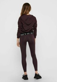 Tmavě burgundová mikina s kapucí na šňůrku, doplněná o odpovídající legíny s bočními panely a elastickým pasem s logem.