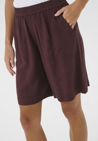 Shorts en coton bordeaux avec une taille élastique, deux poches avant et une coupe décontractée, dotés d'un ourlet qui atteint le milieu de la cuisse.