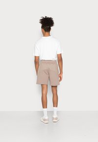 Herrers ljusbruna shorts med mjuk textur och elastisk midja, kombinerat med en enkel vit t-shirt och vita strumpor.