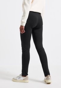 Svarta, kroppsnära leggings av stretchigt material, med hög midja och ankellång design, kombinerade med vita sneakers.