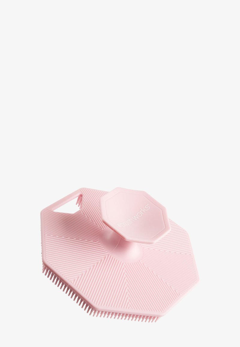 Oktagonal pink silikone skrubber med bløde børster, et hævet håndtag på toppen og en lille indbygget spatel på den ene side.