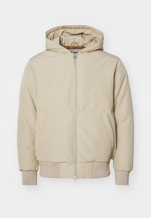 Beige kapucnis dzseki, elülső cipzárral, két nagy oldalsó zsebbel, bordázott mandzsettával és alsó szegéllyel, textúrált anyagból készült. Egyszerű, modern dizájn.