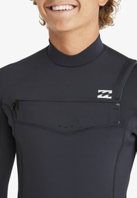 Czarny neoprenowy skafander z wysokim kołnierzem, gładką fakturą, przednią kieszenią na zamek oraz detalem w postaci logo na piersi.