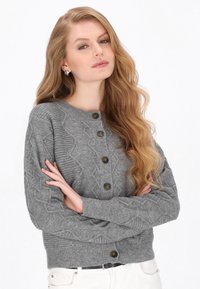 Grau gestrickte Strickjacke mit Zopfmuster, rundem Ausschnitt und fünf dunklen Knöpfen. Mit gerippten Bündchen und Saum sowie strukturierten Details.