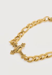 Βραχιόλι από χρυσή αλυσίδα με διακοσμητικό σταυρό χαραγμένο με τη λέξη "Los Angeles" σε λευκό φόντο.