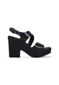 Sandalias cuña negras con parte superior de cuero. Las características incluyen tiras anchas, un hebilla ajustable en el tobillo y una plataforma texturizada con estrías horizontales.