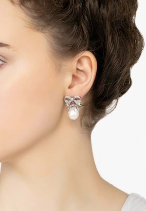 Silver earrings featuring a bow design with clear rhinestones and a white pearl drop. Smooth texture with shiny accents.