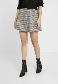 Gonna corta a scacchi bianca e nera con design svasato, abbinata a stivaletti neri attillati alla caviglia con tacco a blocco e dettagli con zip.