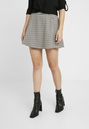 Gonna corta a scacchi bianca e nera con design svasato, abbinata a stivaletti neri attillati alla caviglia con tacco a blocco e dettagli con zip.