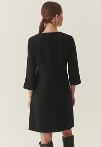 Zwarte jurk van middellange lengte met driekwartmouwen, een rechte snit en een ronde halslijn. Heeft een gladde textuur en een minimalistisch ontwerp.
