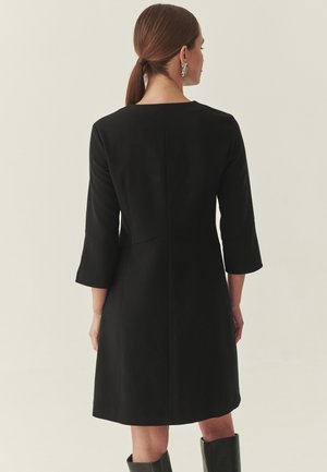 Vestito nero di lunghezza media con maniche a tre quarti, taglio dritto e scollo a barca. Presenta una texture liscia e un design minimalista.