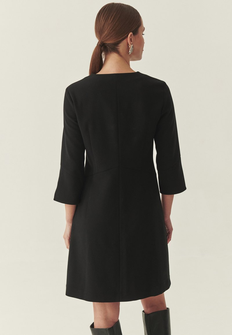 Zwarte jurk van middellange lengte met driekwartmouwen, een rechte snit en een ronde halslijn. Heeft een gladde textuur en een minimalistisch ontwerp.