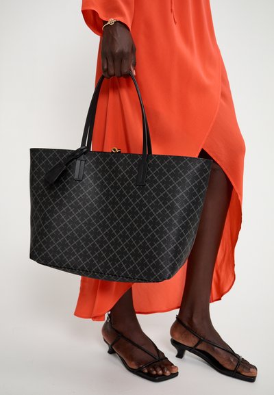Sac fourre-tout noir avec une surface texturée, présentant des motifs gris diagonaux et des anses noires. Le sac est tenu aux côtés d'une robe orange vive.