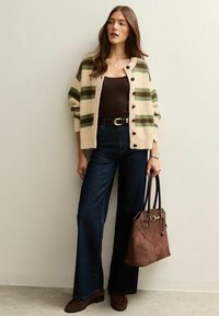 Cremefarbener Cardigan mit grünen Streifen, braunes Tanktop, hochgeschnittene dunkle Jeans, braune Wildlederhandtasche und passende Loafer.
