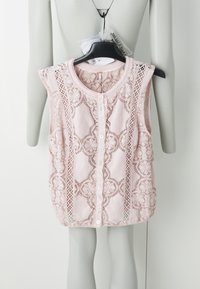 Haut sans manches rose avec des détails en dentelle raffinés, col rond et fermeture à boutons sur le devant. Fabriqué en tissu léger, présenté sur un cintre.