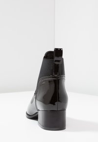 Bottine en cuir verni noir avec panneaux latéraux élastiques et petit talon carré ; texture lisse avec une finition brillante et languette de tirage à l'arrière.