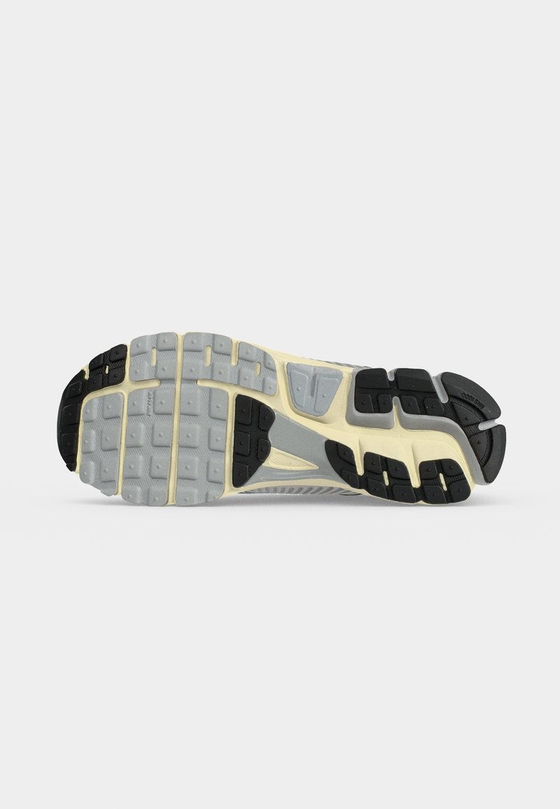 Suela de una zapatilla de correr que muestra suela gris y negra con patrones segmentados de agarre y una entresuela beige.