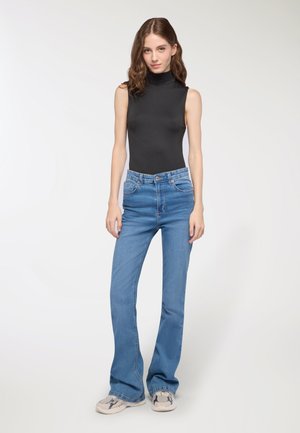 Body scollato nero senza maniche con collo alto, abbinato a jeans svasati azzurri. I jeans presentano tasche frontali e un classico design con passanti per la cintura.