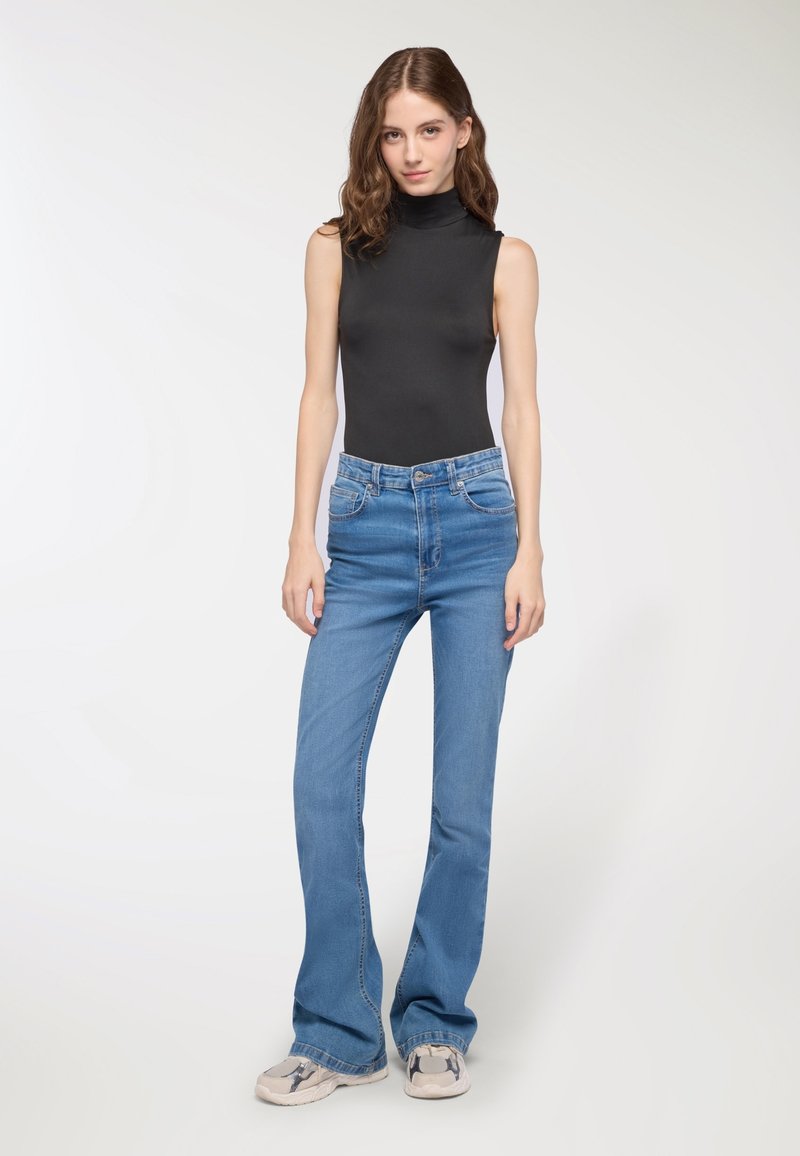 Body scollato nero senza maniche con collo alto, abbinato a jeans svasati azzurri. I jeans presentano tasche frontali e un classico design con passanti per la cintura.
