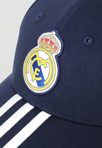 Mørkeblå caps laget av bomull, med et rundt logo med en krone og initialene "RM", samt tre hvite vertikale striper front.