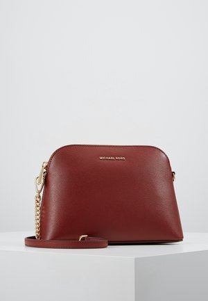 Brązowa, teksturowana skórzana torba na ramię Michael Kors z złotym łańcuszkiem i zamkiem błyskawicznym, prezentowana na białym postumencie na szarym tle.