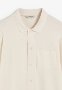 Polohemd aus cremefarbener Baumwolle, mit klassischem Kragen, Knopfverschluss, subtiler Struktur und einer einzelnen Brusttasche.