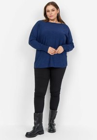 Granatowy sweter z dzianiny z szerokim dekoltem i długimi rękawami, połączony z dopasowanymi czarnymi spodniami i czarnymi skórzanymi botkami za kostkę.