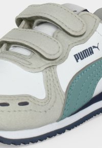 White and beige Puma sneaker with teal logo and dual hook-and-loop straps on top for fastening.