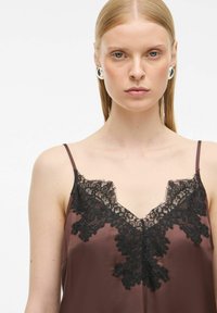 Brązowa satynowa koszulka na ramiączkach z czarną koronką na dekolcie w kształcie litery V i cienkimi ramiączkami. Posiada gładką teksturę i delikatne koronkowe wykończenie.