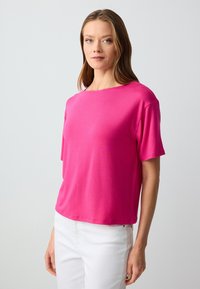T-shirt a maniche corte e collo rotondo di un vivace colore rosa, realizzato in tessuto morbido, con una vestibilità comoda e una texture liscia. Indossato con jeans bianchi.