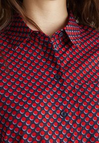 Camicia a maniche lunghe rossa e blu con un motivo circolare in colori contrastanti, colletto regolare e taschino frontale. Tessuto con una texture liscia.