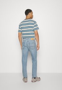 T-shirt a righe blu, crema e navy; jeans blu con vestibilità classica; sneakers con una base grigia e accenti rossi.