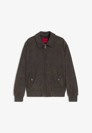 Donkerbruine suède bomberjack met ritssluiting aan de voorkant, klepzakken met knopen, geribbelde boorden en zoom, en een rood binnenlabel met de tekst "HUGO".