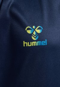 Tissu sportif bleu avec un logo de colibri jaune et bleu au-dessus du mot « hummel » imprimé dans des couleurs assorties.
