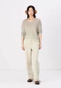 Maglione a maglia beige con scollatura a V, vestibilità ampia e texture a coste. Abbinato a pantaloni palazzo beige chiaro e scarpe scivolate scure.