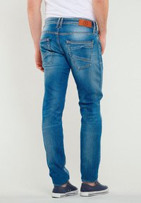 Blauwe denim jeans met een tapered fit, voorzien van achterzakken, een bruine leren patch op de tailleband en subtiele vervaging op de stof.