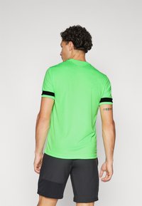 Lys grønn kortermet t-skjorte med svarte detaljer på ermene, laget av glatt stoff. Bakfra viser den et enkelt, tettsittende design.