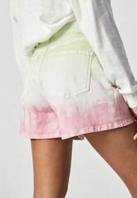 Denimshortsit on liukuvärjättyjä, vaalean vihreästä vaaleanpunaiseen. Takana on taskut ja suora leikkaus. Valkoinen yläosa osittain näkyvissä.