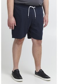 Marineblaue Baumwollshorts mit einem elastischen Bund und weißem Kordelzug. Ein Paar schwarze Sneakers mit weißen Sohlen. Schlichtes Design, keine Muster.