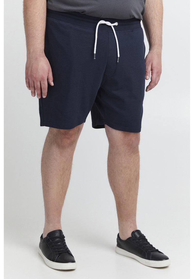 Marineblaue Baumwollshorts mit einem elastischen Bund und weißem Kordelzug. Ein Paar schwarze Sneakers mit weißen Sohlen. Schlichtes Design, keine Muster.
