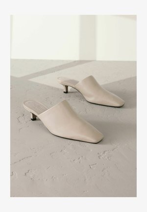 Beige bőr mules, hegyes orral és alacsony fekete sarokkal. Simább textúra, slip-on kialakítás, minimalista sziluett, látható minták nélkül.