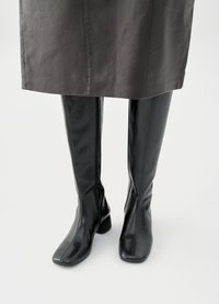 Juodi iki kelių batai iš lygios odos, suapvalintu noseliu ir nedideliu blokuota kulnu, su formą prilaikančia siluete.